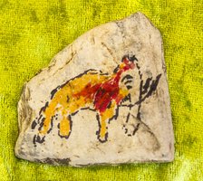 Ein bemalter Stein zeigt ein Tier, möglicherweise ein Pferd, in Gelb- und Rottönen mit schwarzen Konturen, das auf einer strukturierten, hellgrünen Fläche abgebildet ist.