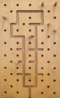 Eine Holzstecktafel mit vielen Löchern und mehreren Stiften, in deren Mitte ein schlüsselförmiger Pfad in das Brett geschnitzt ist.