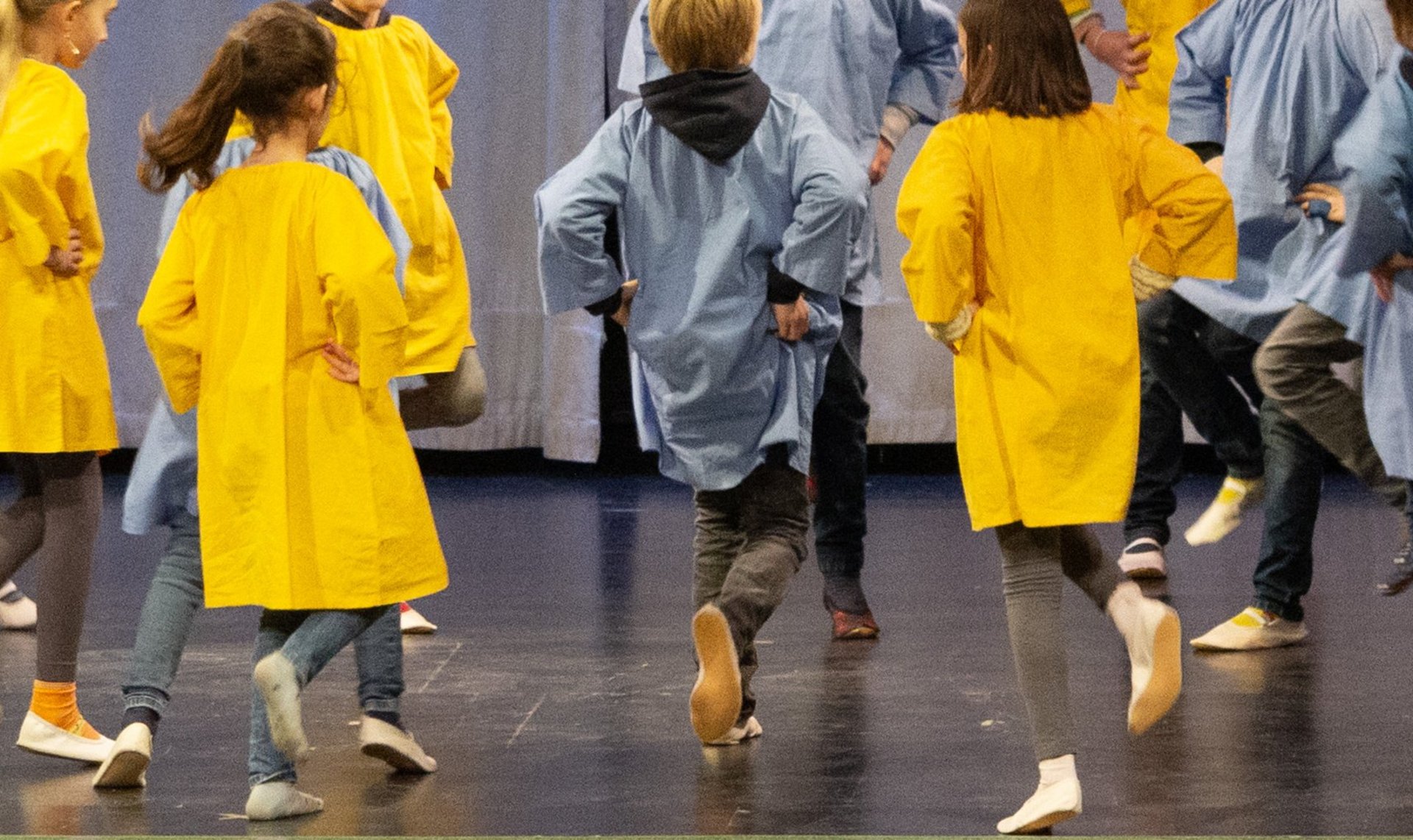 Kinder spielen draußen, lächeln und halten sich an den Händen, während sie im Kreis stehen; im Hintergrund sind Bäume und Gebäude zu sehen – an einem sonnigen Tag.