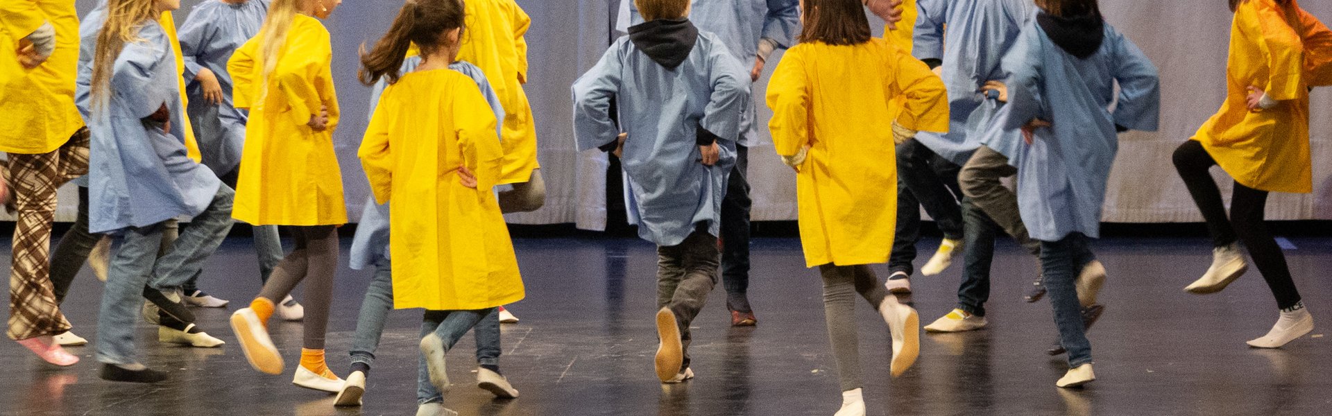 Kinder spielen draußen, lächeln und halten sich an den Händen, während sie im Kreis stehen; im Hintergrund sind Bäume und Gebäude zu sehen – an einem sonnigen Tag.